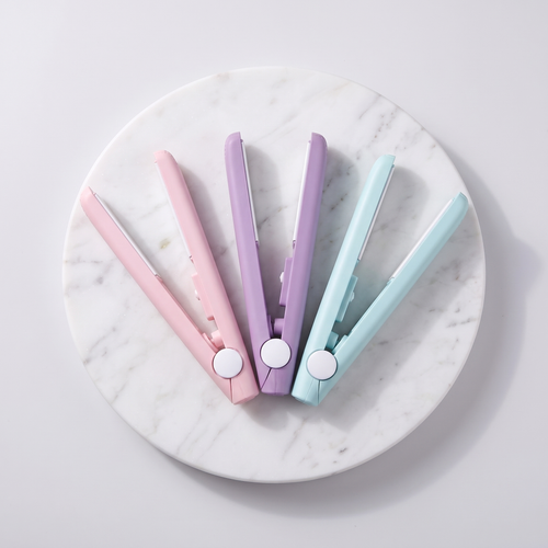 Three mini flat iron hair straighteners in pastel pink, purple and mint on marble